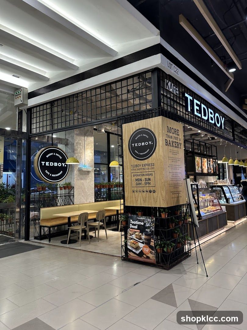 The exterior of a Tedboy cafe and restaurant with prominent signage. The storefront features a black metal frame with glass panels, a light-colored counter, and booth seating visible inside. A large circular sign with the Tedboy logo is mounted on the left side of the entrance. A wooden pillar displays the cafe's name, operating hours, and a "Teatime Deal" advertisement.
