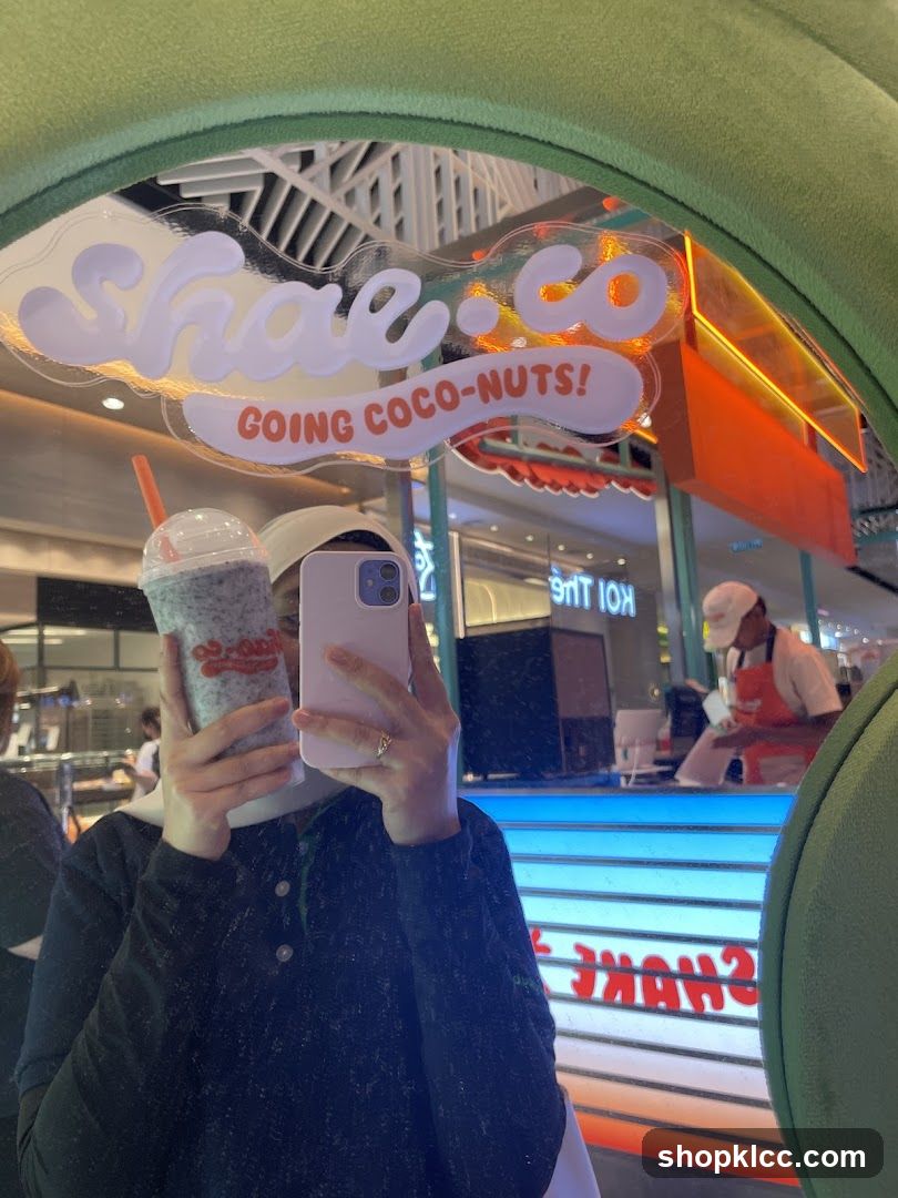 Person holding a drink in front of a mirror reflecting a shop