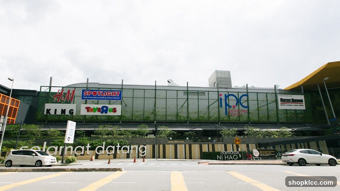 A wide shot of a shopping center facade with various store signs visible, including H&M, SPOTLIGHT, Toys R Us, KING, IPC Shopping Center, and Harvey Norman. The text "selamat datang" is displayed prominently in front of the building.