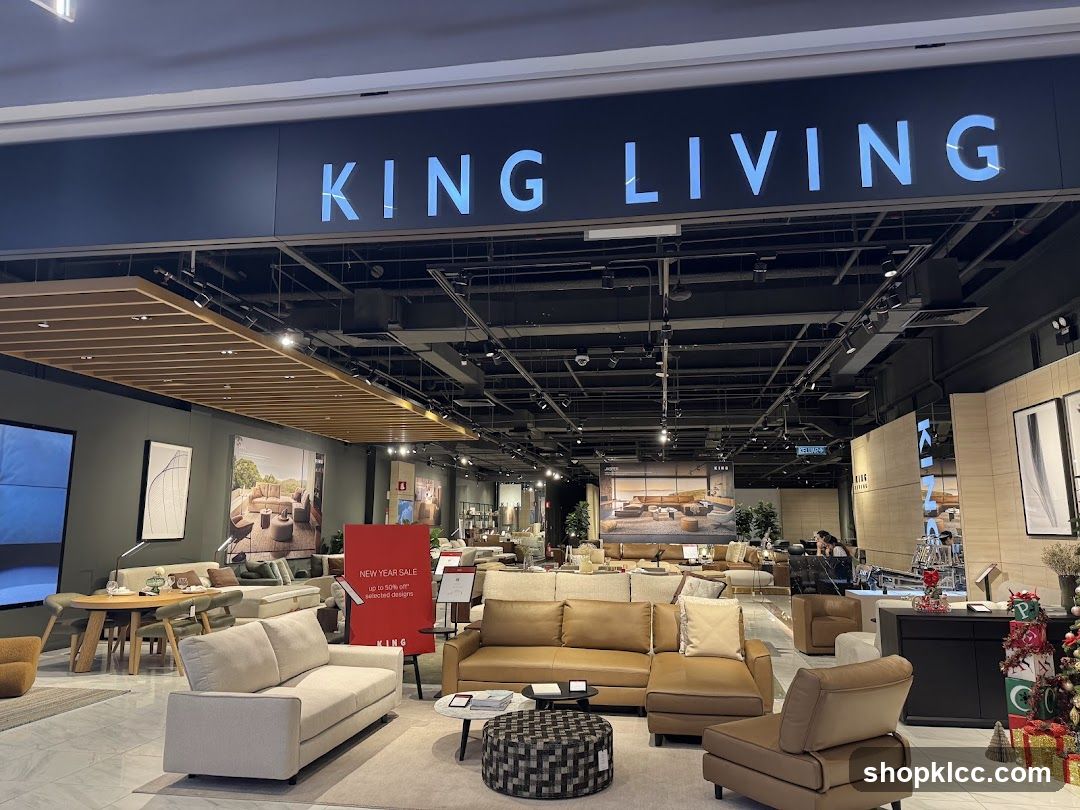 The exterior of a King Living furniture store. The large sign above the entrance reads "KING LIVING" in illuminated blue letters. Inside, various sofas, chairs, and dining sets are displayed. A red sign in the foreground advertises a "NEW YEAR SALE" with up to 50% off selected designs.
