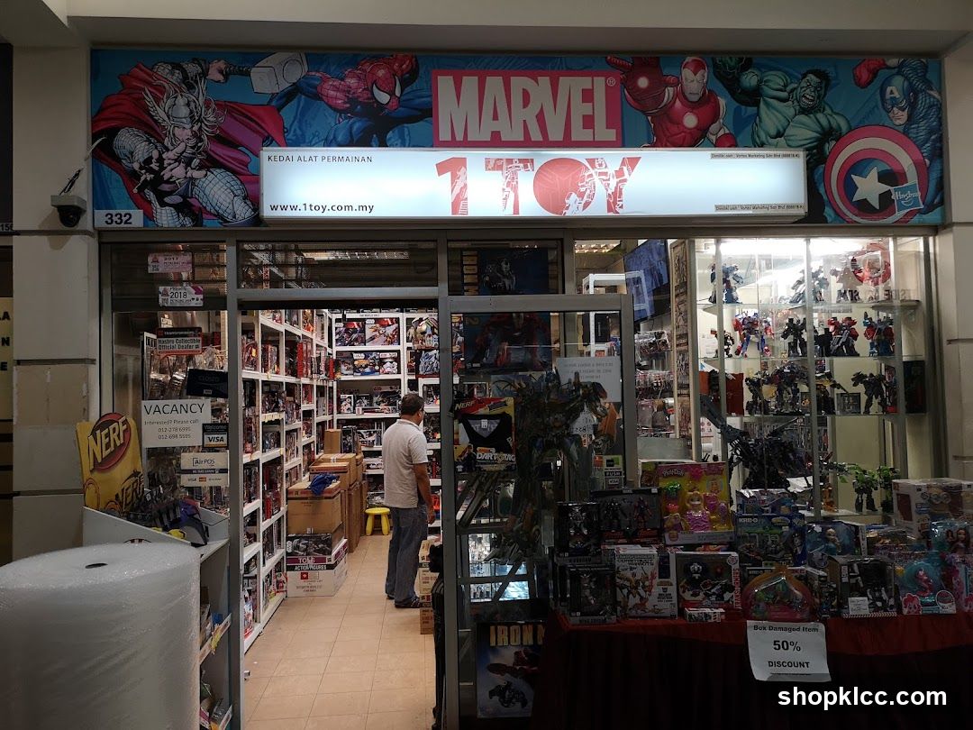 The storefront of a toy store with a large Marvel-themed mural above the entrance. The store's name, "1TOY", is prominently displayed. Inside, shelves are stocked with various toys and action figures. A sign indicates a 50% discount on box-damaged items.