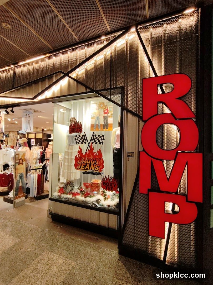The exterior of a clothing store with large red letters spelling out "ROMP" on the right side. The storefront features a display window showcasing mannequins dressed in clothing, along with festive decorations. Inside, racks of apparel are visible.