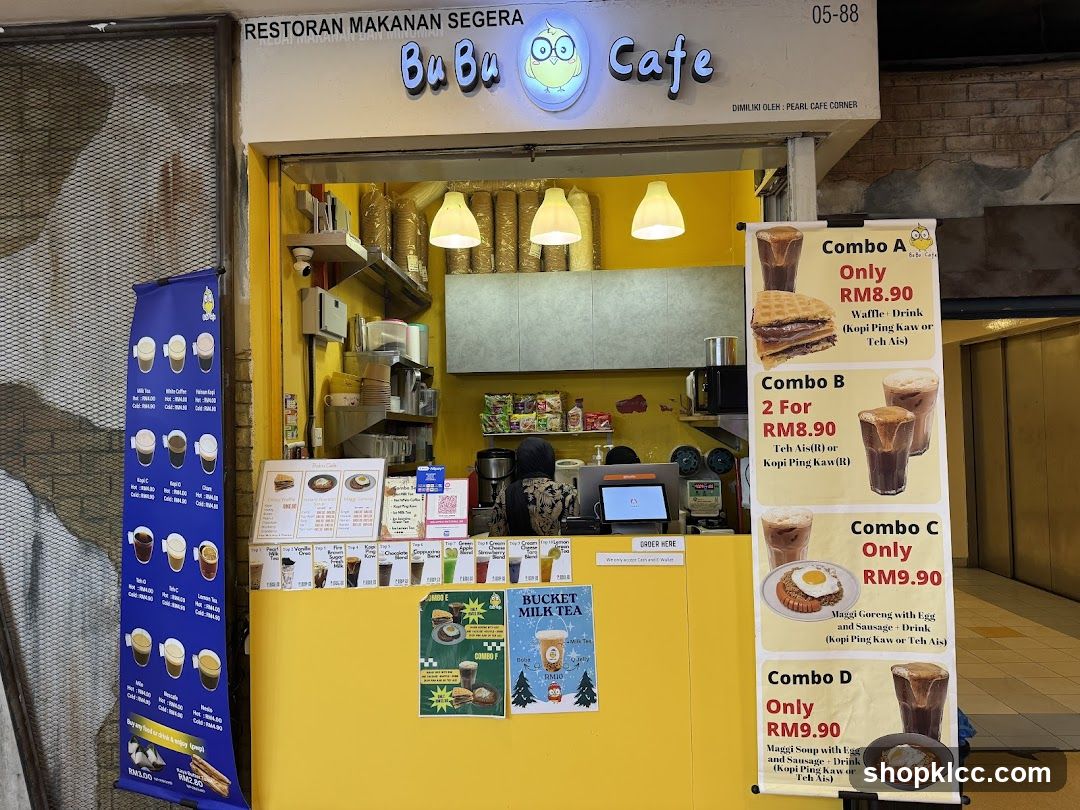 A bright yellow food stall with a sign that reads "RESTORAN MAKANAN SEGERA BuBu Cafe". There are several menu boards and posters displayed. A blue banner on the left shows various drinks. To the right, there are combo meal advertisements. The stall appears to be open for business.