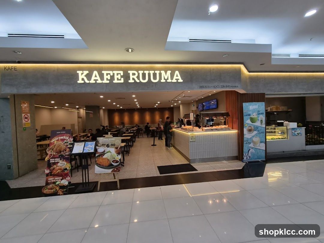 The storefront of Kafe Ruuma is visible with illuminated signage above the entrance. The interior shows a modern dining area with tables, chairs, and a counter where staff are present. The floor is tiled, and ceiling lights illuminate the space.