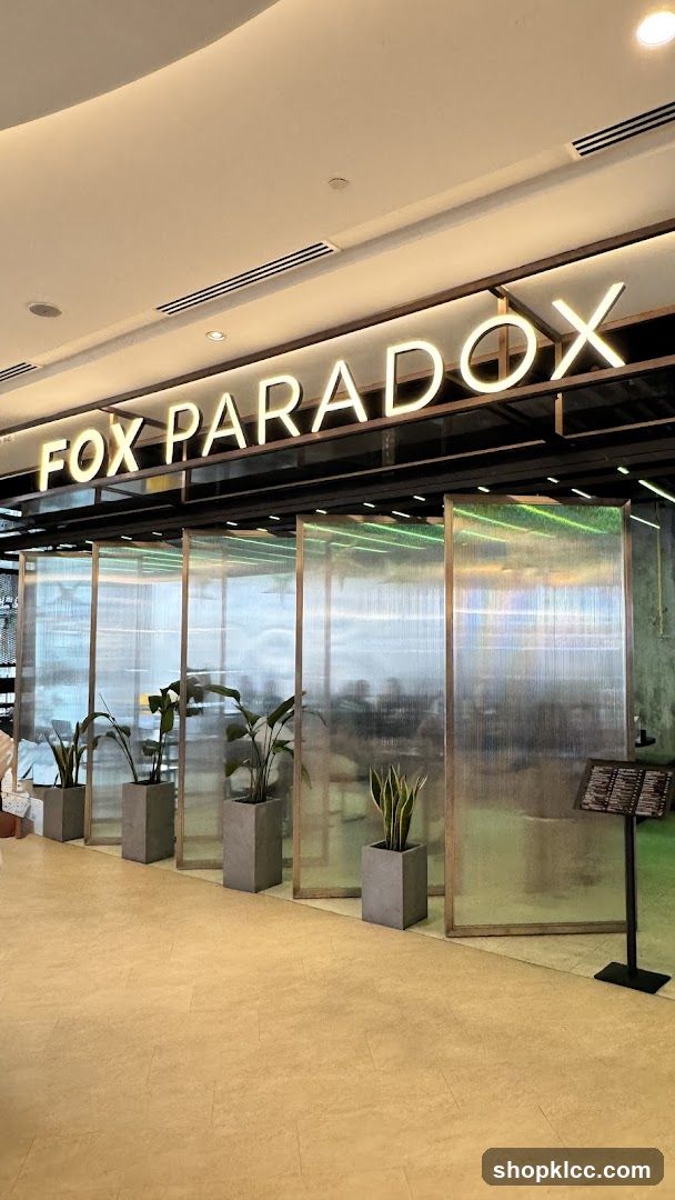 The exterior of a modern establishment with the name "FOX PARADOX" displayed in illuminated neon letters above a series of translucent, ribbed panels. Potted plants are placed in front of the panels, adding a touch of greenery. A menu stand is visible to the right.
