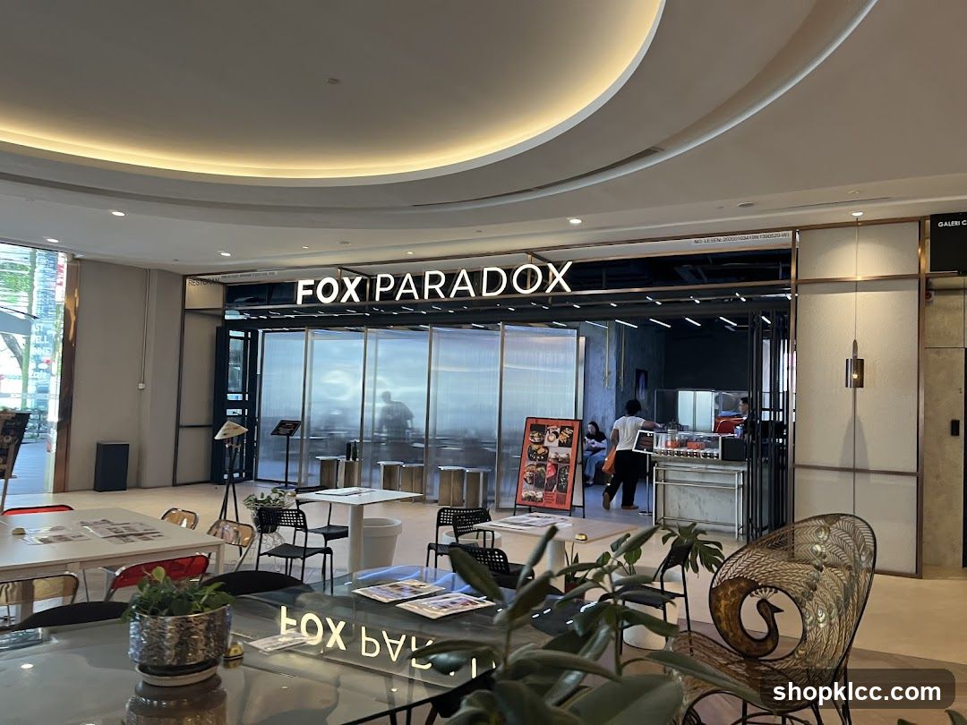 The exterior of a restaurant called Fox Paradox. The restaurant has large glass windows and a prominent sign above the entrance. Inside, tables and chairs are visible, along with some patrons and staff. There are also some decorative elements and plants in the foreground.