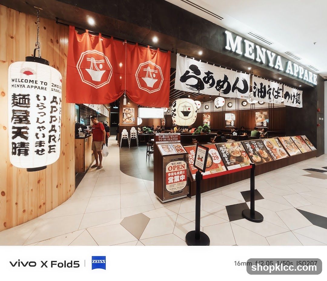 The exterior of a ramen restaurant with Japanese-style lanterns and banners. The restaurant's name,