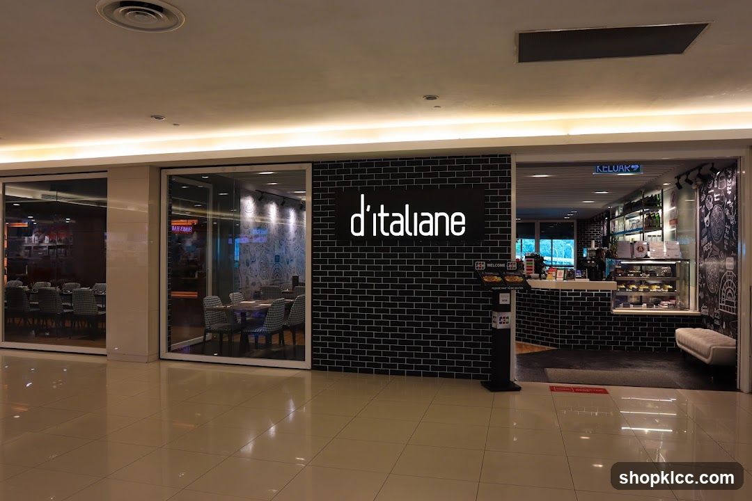 The exterior of a D'Italiane restaurant with a black brick facade. A large illuminated sign with the restaurant's name is centered on the facade. To the left, large glass windows reveal dining tables and chairs inside. To the right, an open entrance shows a counter area with display cases, shelves stocked with bottles, and a menu stand. A white bench is visible to the right of the entrance.