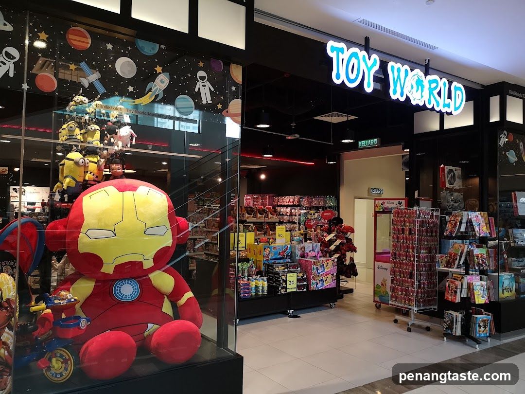 The exterior of a toy store called Toy World. The storefront features a large display window showcasing plush toys, including a giant Iron Man plush. Inside, shelves are stocked with various toys and games. The store's name is prominently displayed in large, illuminated letters above the entrance.
