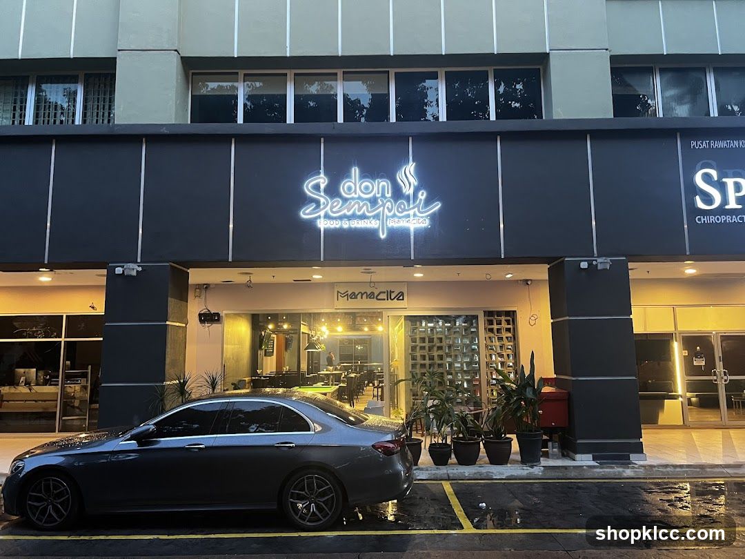 The exterior of a restaurant called Don Sempoi Food & Drink. The restaurant has a neon sign above the entrance. There is a car parked in front of the restaurant.