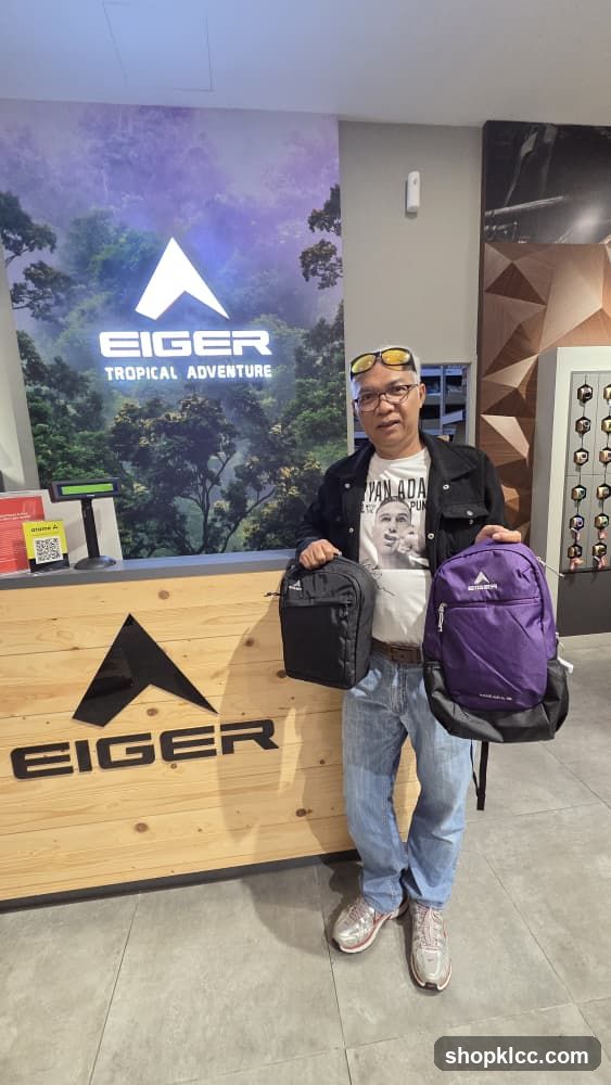 Man holding backpacks in front of Eiger store display