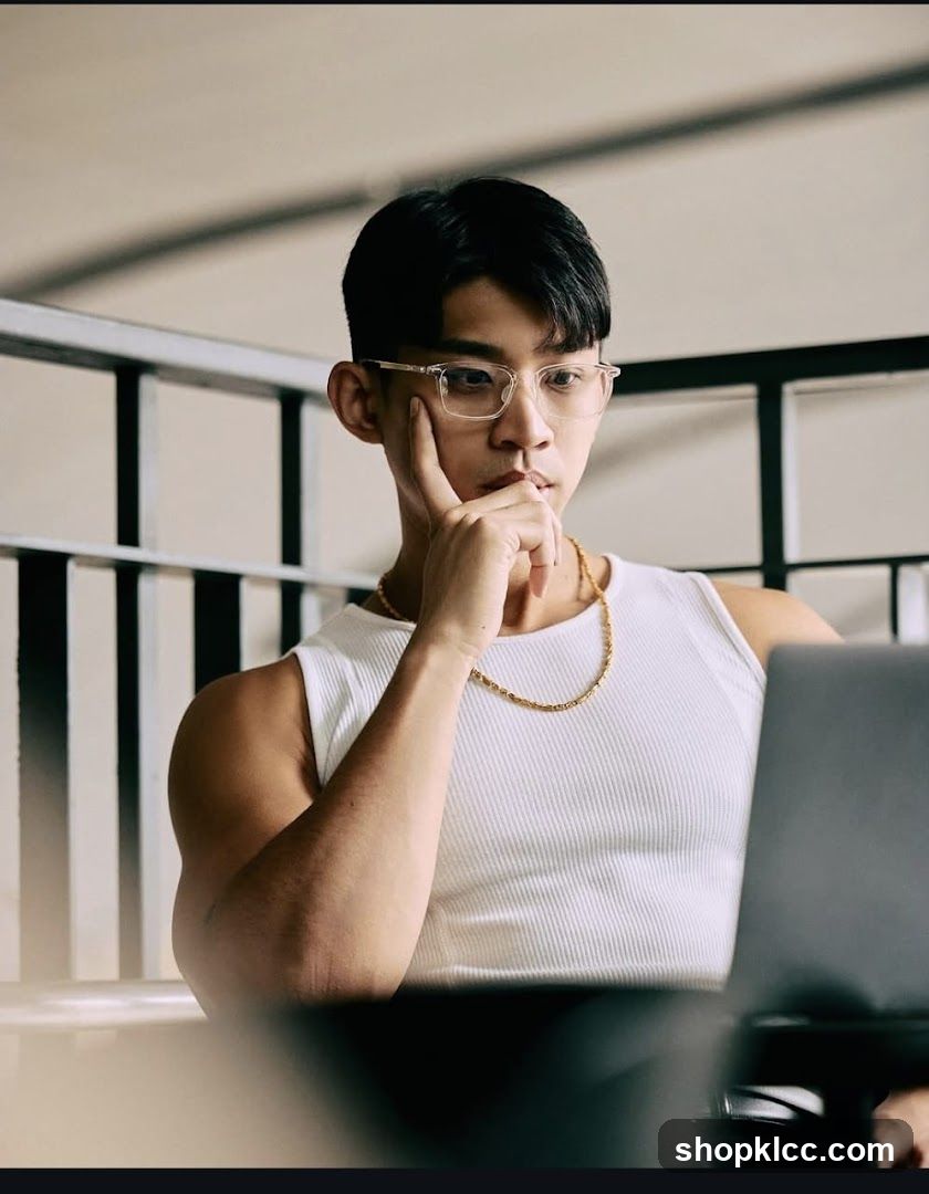Man in white tank top thinking at laptop