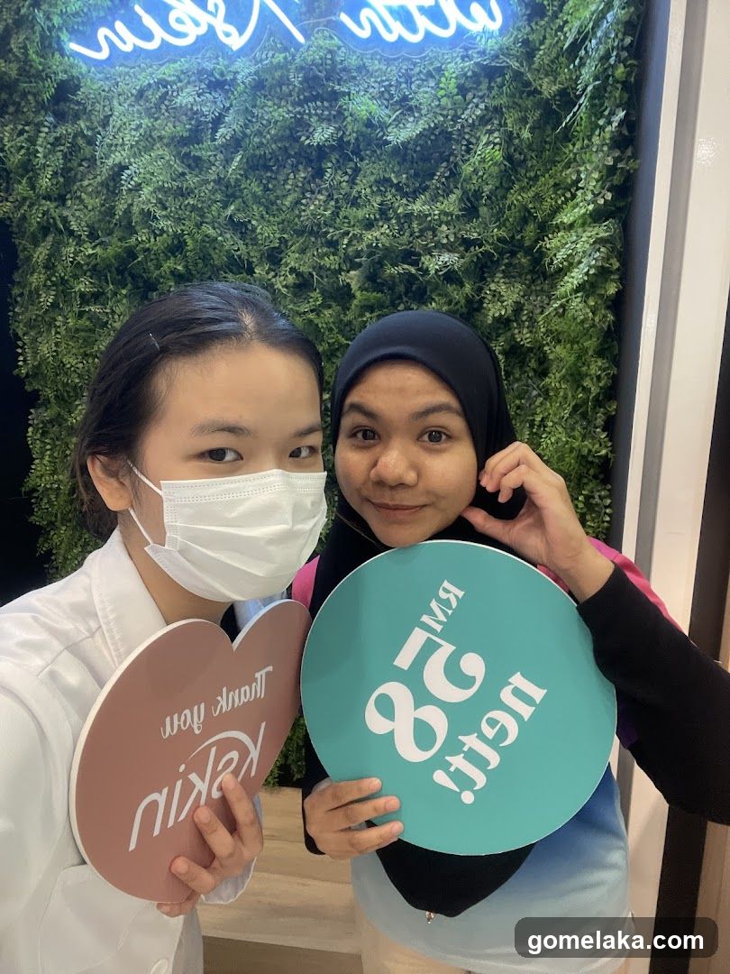 Two individuals holding promotional signs in front of a green wall with neon sign