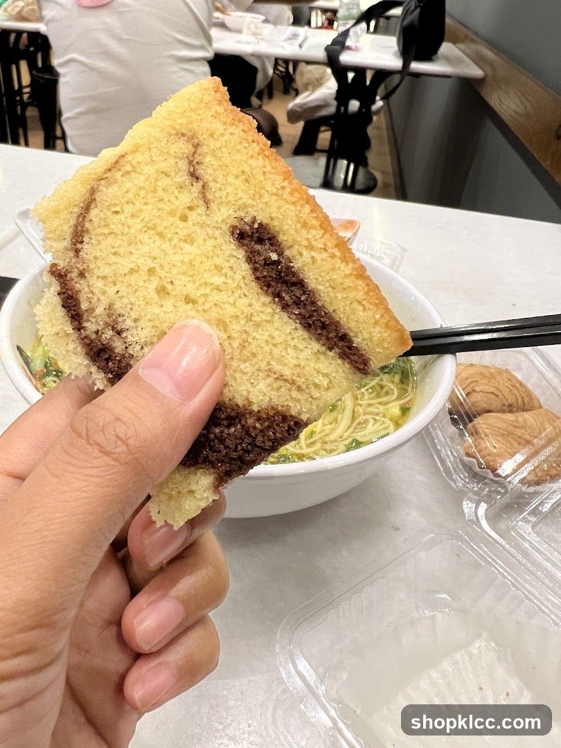 Hand holding cake slice near noodle bowl