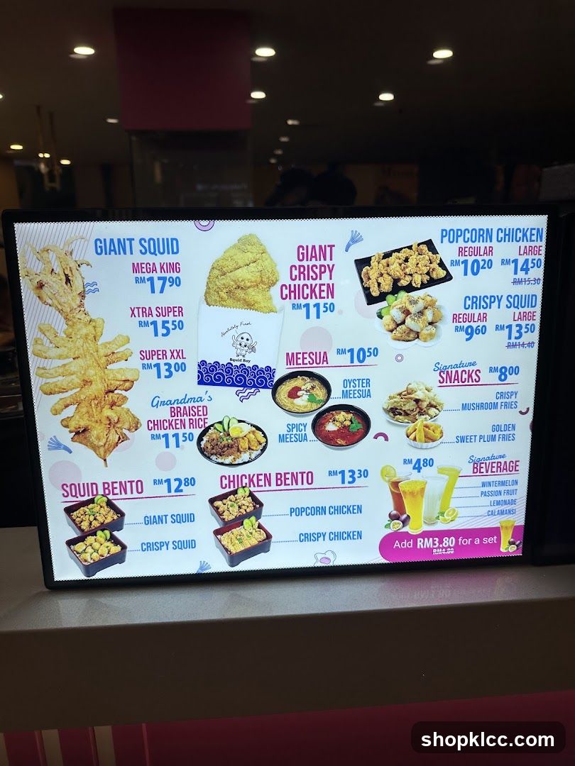 Digital menu board displaying various food items with prices in RM, including Giant Squid, Crispy Chicken, Popcorn Chicken, Squid Bento, and signature snacks.