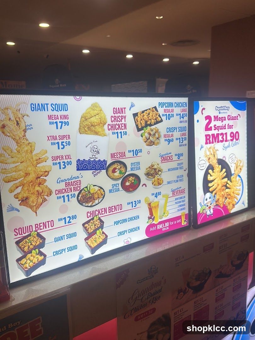 A brightly lit digital menu board displaying fried seafood and chicken items with prices in RM, including Giant Squid, Crispy Chicken, Bento sets, and snacks like popcorn chicken.