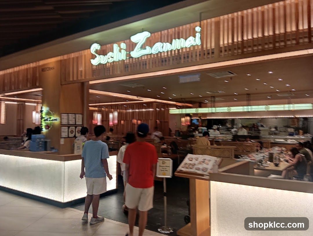 The exterior of a Sushi Zanmai restaurant with its prominent signage. The restaurant features a modern design with wooden accents and bright interior lighting. Several patrons are visible entering and dining inside.