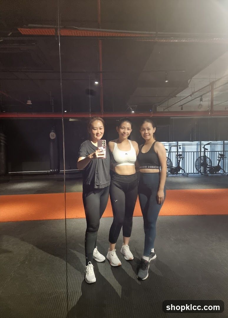 Three women in athletic wear posing for a mirror selfie in a gym.