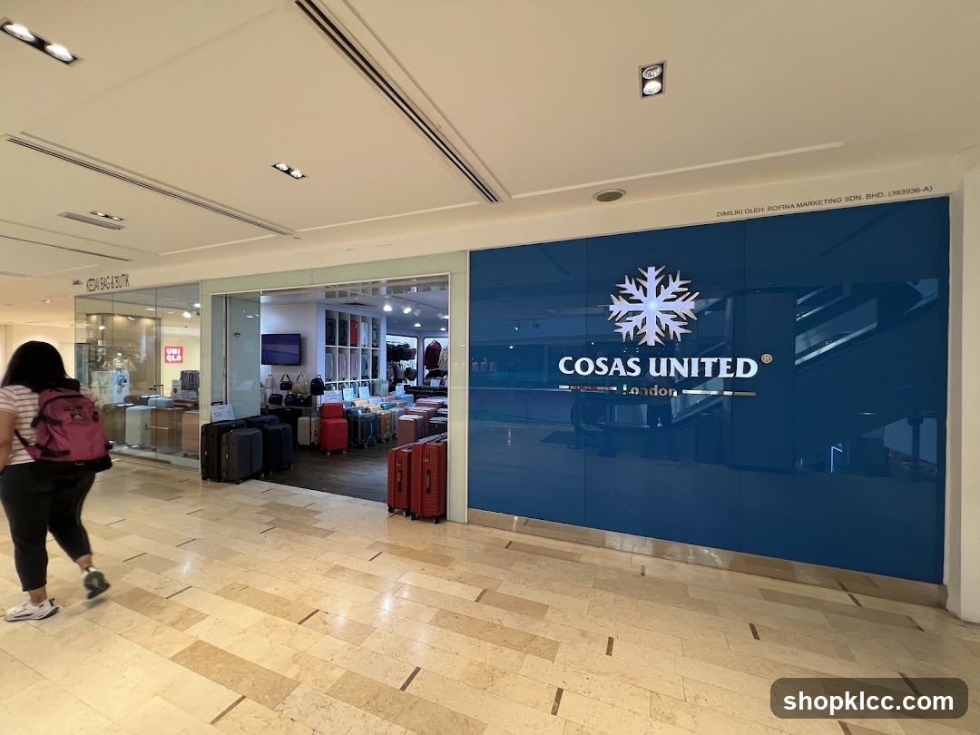 The exterior of a store with a large blue glass facade displaying the "Cosas United London" logo and name. Luggage is displayed outside the entrance. To the left, another store labeled "Kedai Bag & Butik" is visible, with "UNI QLO" signage inside.