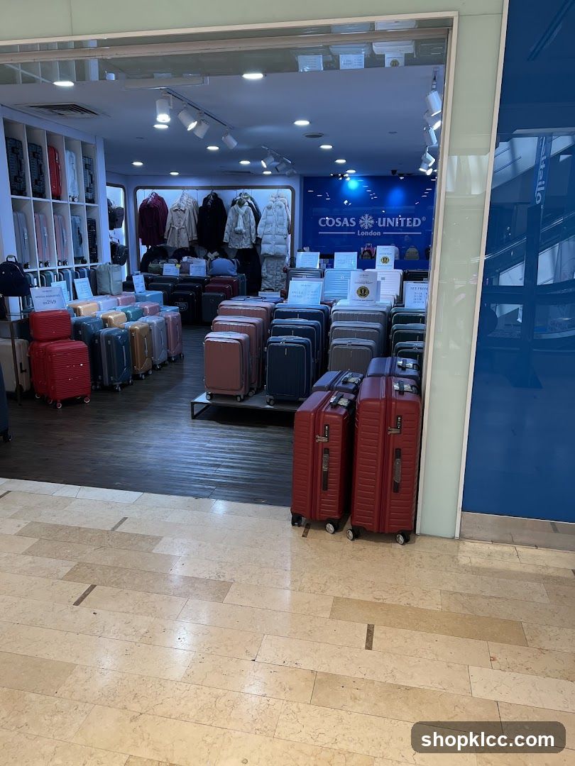 The image shows the entrance to a store selling luggage and outerwear. Racks of suitcases in various colors and sizes are displayed prominently. In the background, coats are hung on a display wall, and a sign with the logo "COSAS UNITED London" is visible. The store appears well-lit and organized, with a wide selection of products.