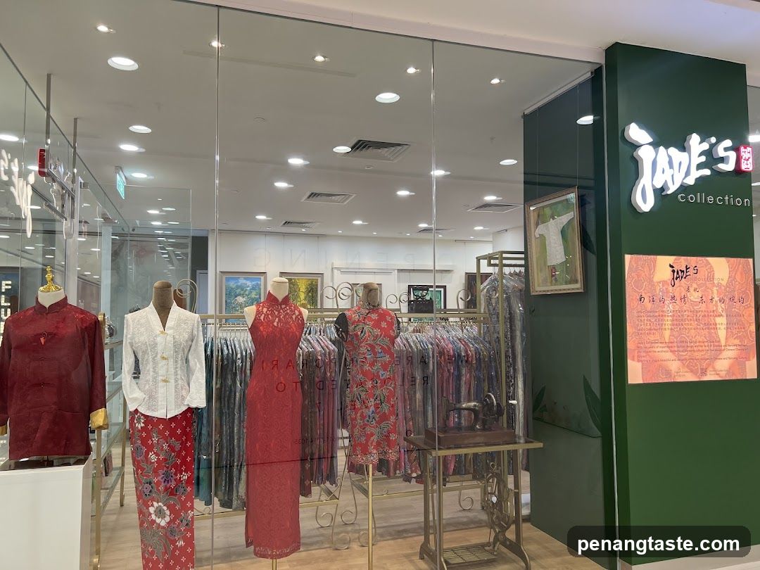 A storefront display featuring traditional Chinese clothing on mannequins and racks. The shop's name, "Jade's Collection," is prominently displayed on a green pillar. A framed artwork and an antique sewing machine are also part of the display. A descriptive plaque is visible on the right side of the entrance.