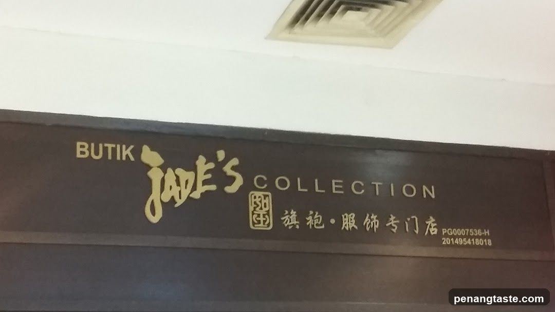 A dark brown sign with gold lettering reads "BUTIK Jade's COLLECTION". Below this, there is a square emblem followed by Chinese characters and then two lines of numbers.