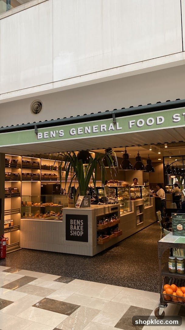 The exterior of Ben's General Food Store, a bakery and food shop. The storefront features a green awning with white lettering that reads "BEN'S GENERAL FOOD STORE". Below the awning, the shop displays baked goods and other food items in glass cases and on shelves. A sign on the counter reads "BENS BAKE SHOP".