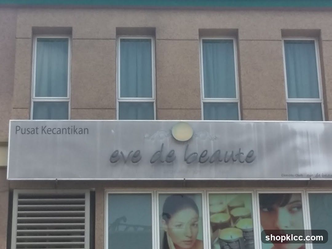 The exterior of a building with a sign that reads "Pusat Kecantikan eve de beaute". Below the sign are windows displaying images of women and candles.