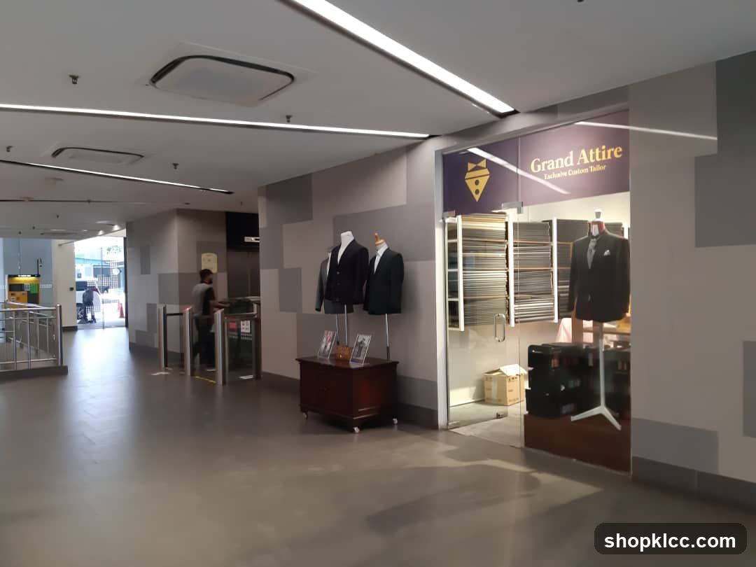 The entrance to a tailor shop called Grand Attire. The shop has a glass front with the name and logo displayed. Inside, shelves are stocked with fabric swatches, and a mannequin wears a suit.