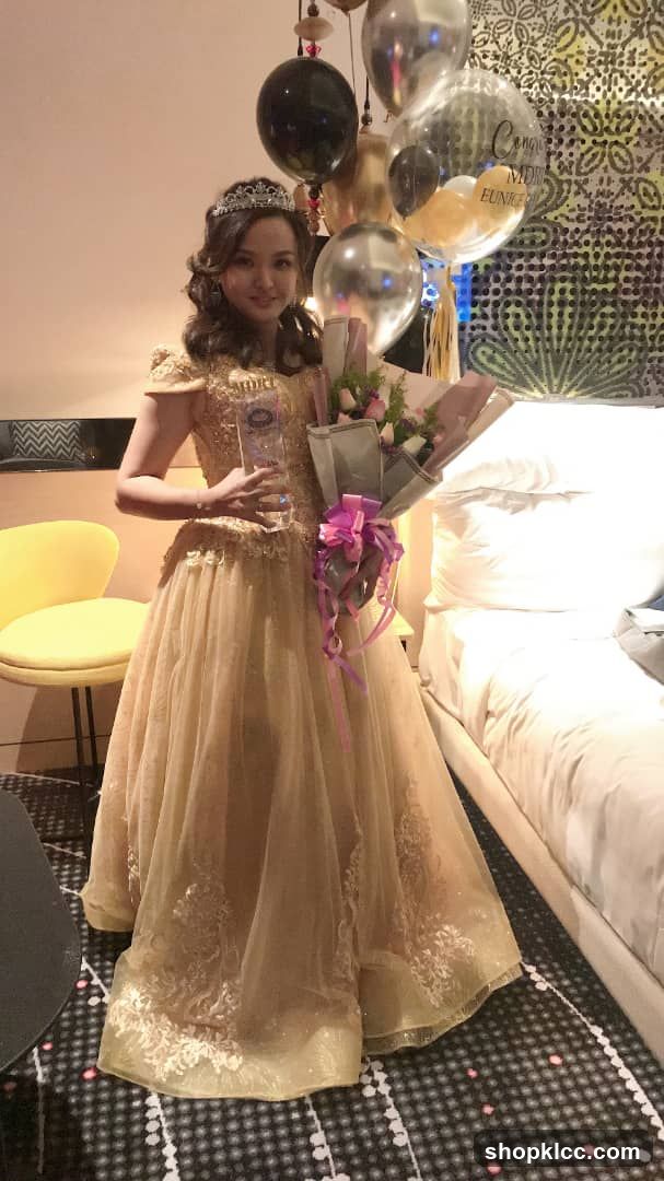 Woman in a formal gown holding a trophy and flowers