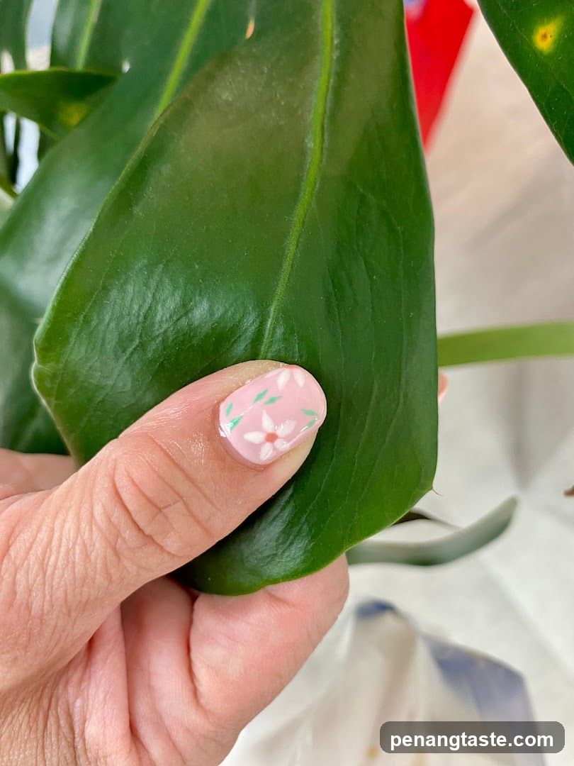 Close-up of a hand with floral nail art touching a large green leaf