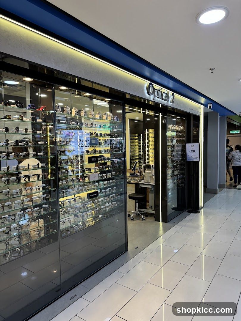The storefront of an optical shop named Optical 2. The shop has large glass display windows showcasing numerous eyeglasses. Inside, there are more displays of eyewear, an examination chair, and a price board.