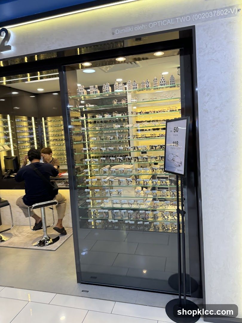 The exterior of an optical store with a large glass display window showcasing numerous eyeglasses on shelves. A sign is visible on a stand outside the window. Inside, two people are seated at a counter.
