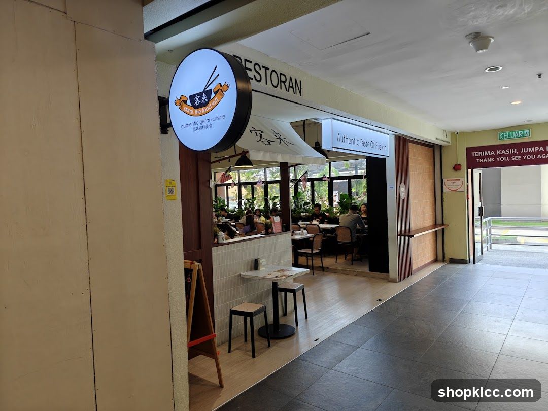 The exterior of a restaurant with a circular sign displaying "gerai, the food loft authentic gerai cuisine" and a rectangular sign that reads "Authentic Taste Of Fusion". The restaurant interior is visible with patrons seated at tables.